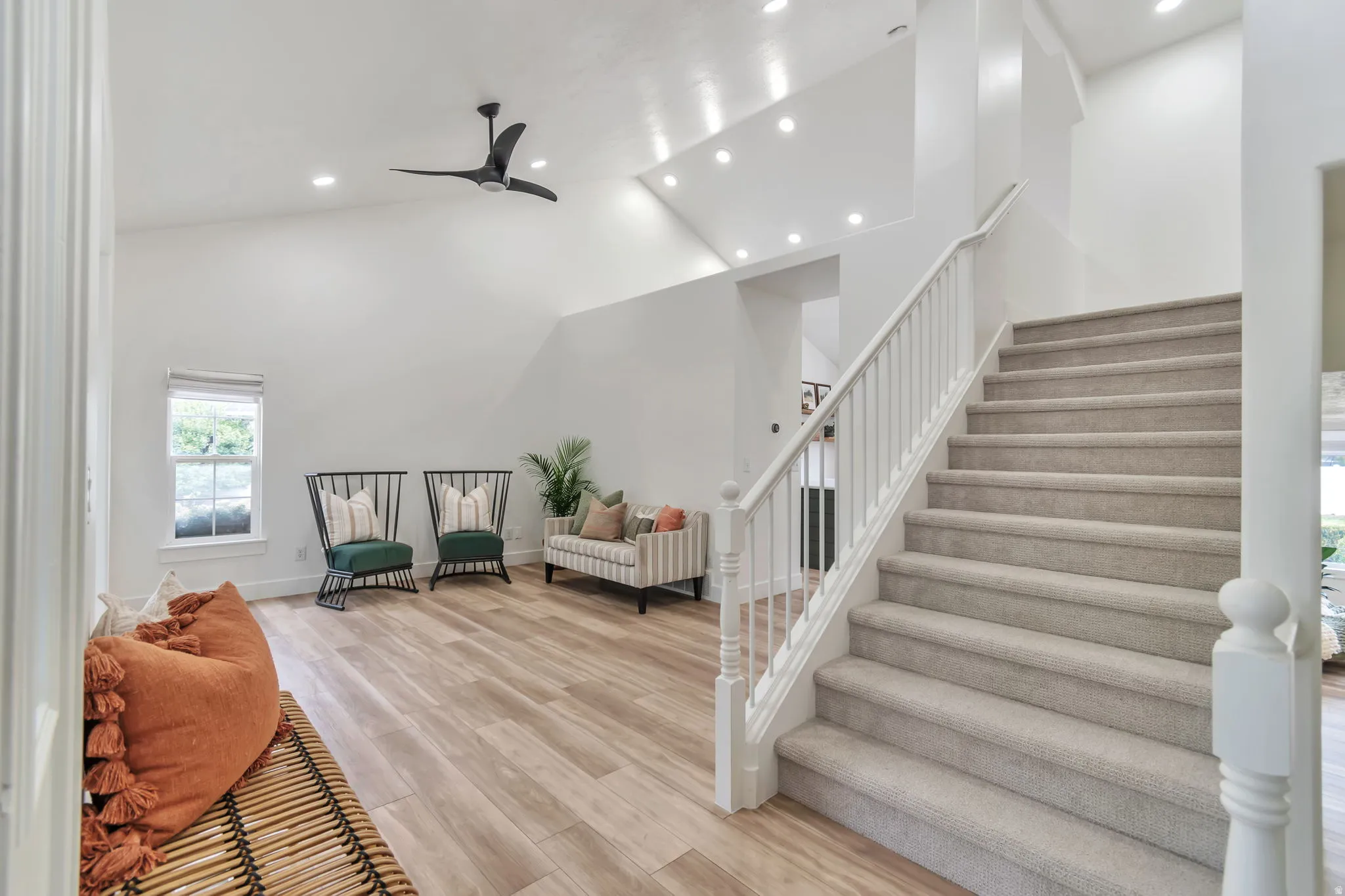 Vaulted ceilings with recessed lighting, wood-finish flooring, white painted staircase with carpeted treads, and a black ceiling fan