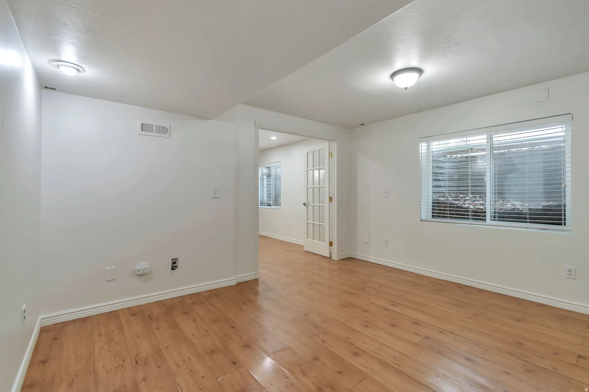 Light wood-finish flooring, white walls, recessed lighting, and a white interior door with glass panels