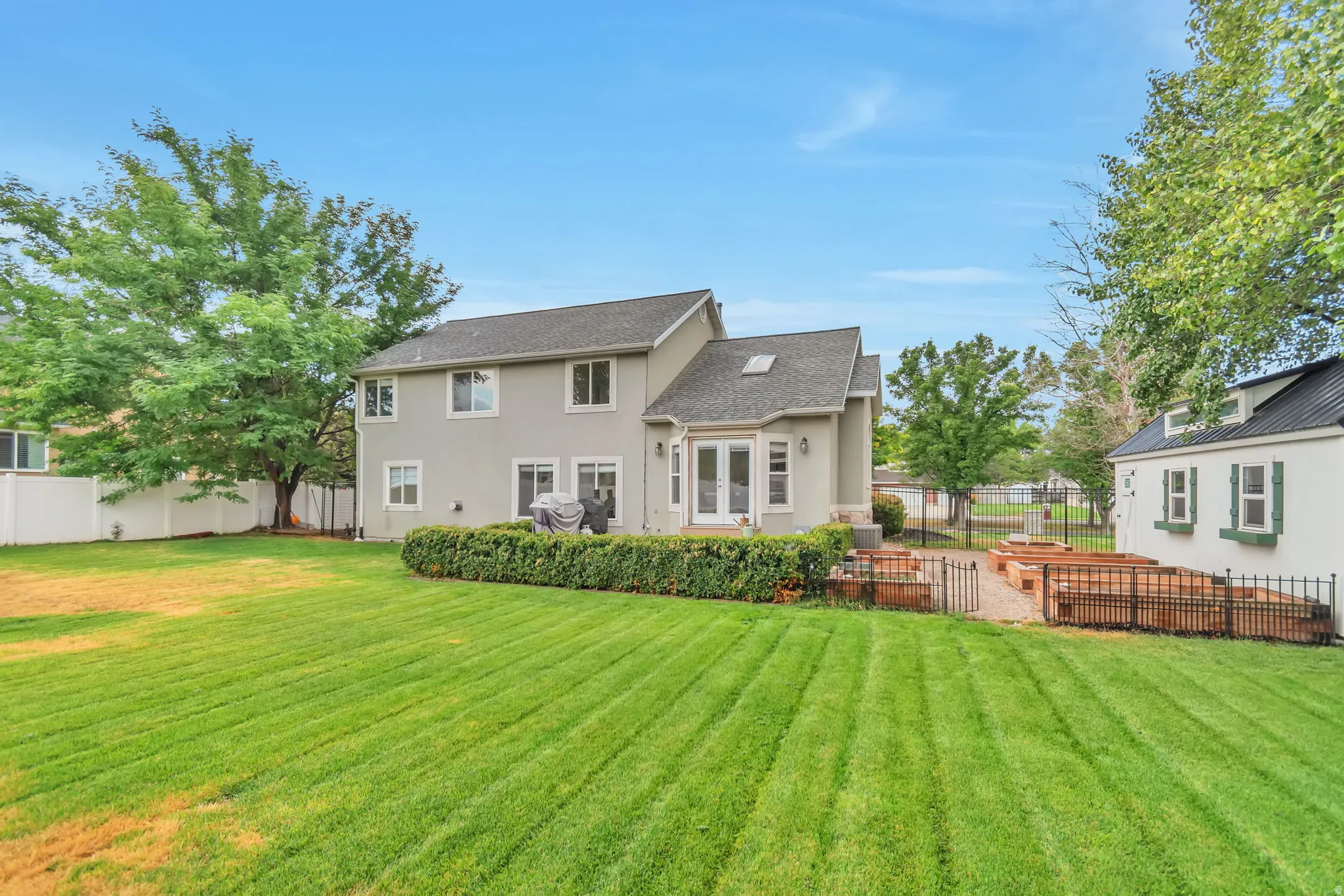 Expansive lawn, patio access, detached shed, raised garden beds, and mature trees
