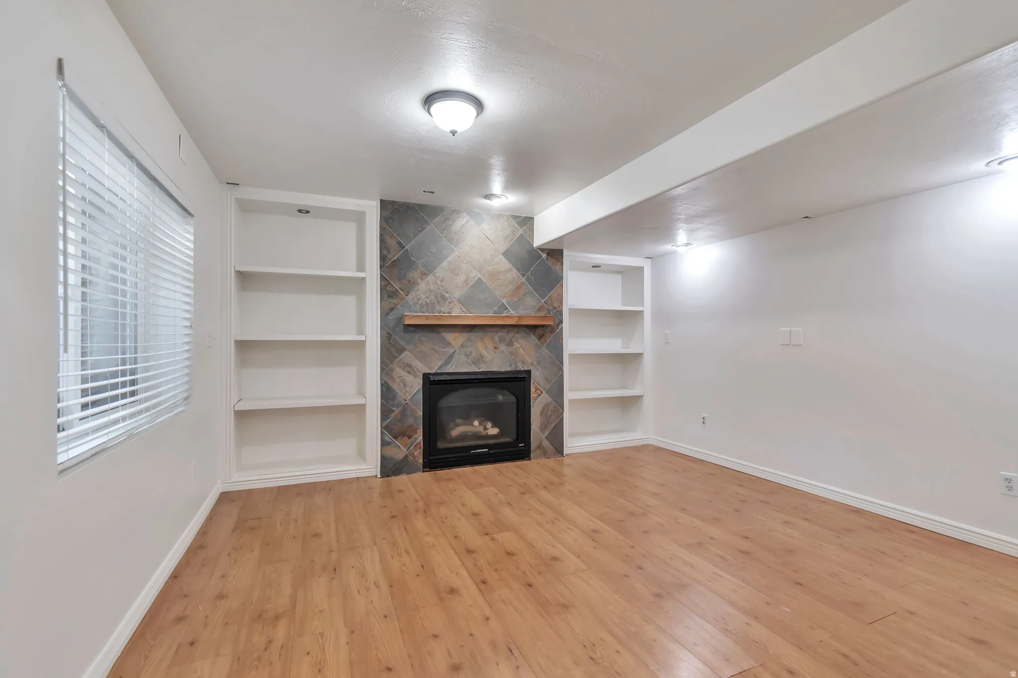 Living area featuring wood-finish flooring, a fireplace with a stone tile surround, a wood mantle, and built-in shelving