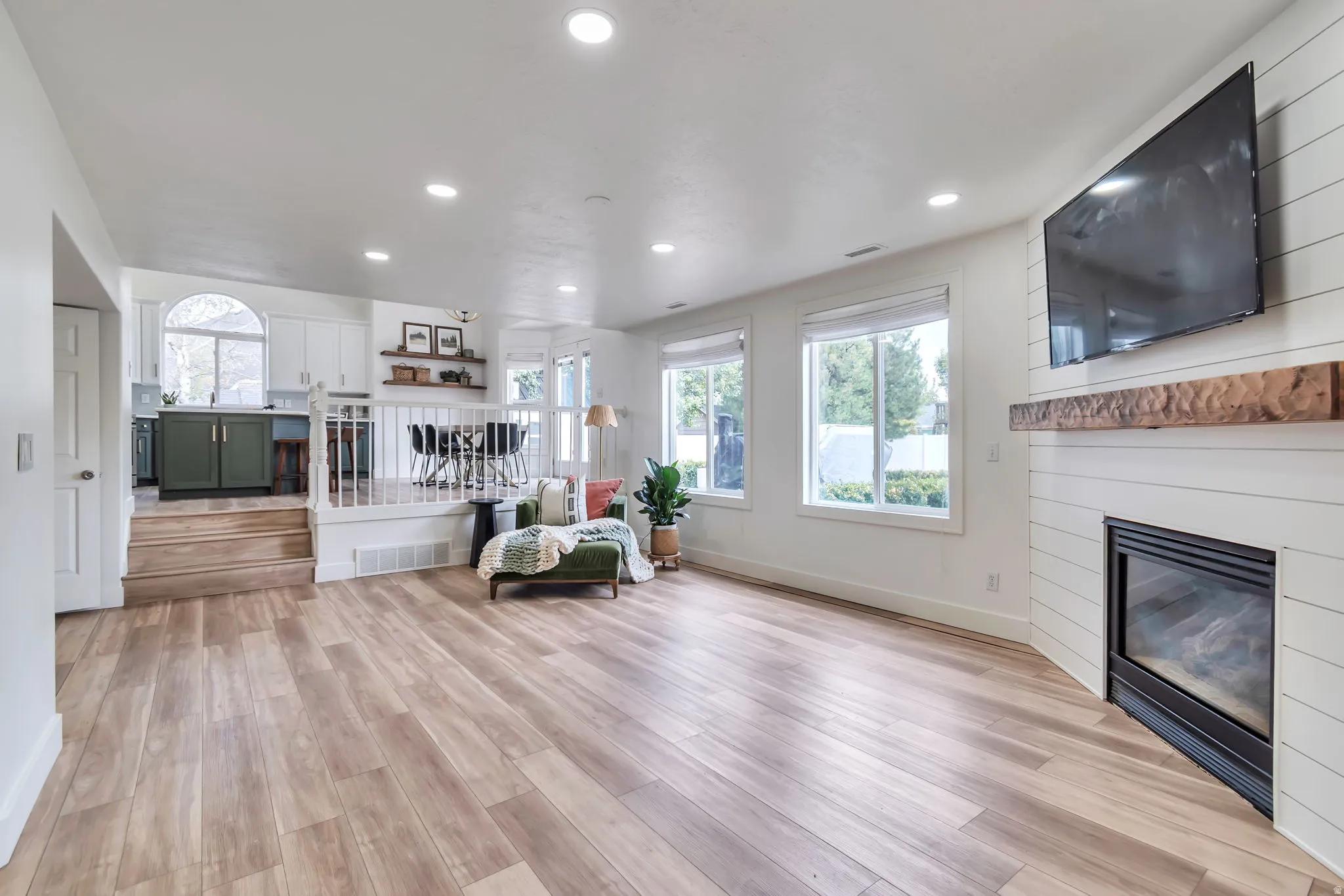 Wood-finish flooring throughout, recessed lighting, and a corner fireplace with a shiplap surround and a wood mantel