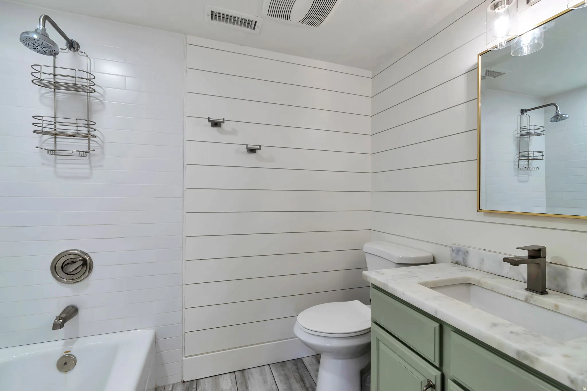 Bathroom featuring a white subway tile tub surround, shiplap wall paneling, a single vanity with a light green cabinet, a rectangular undermount sink, and a gold-framed mirror