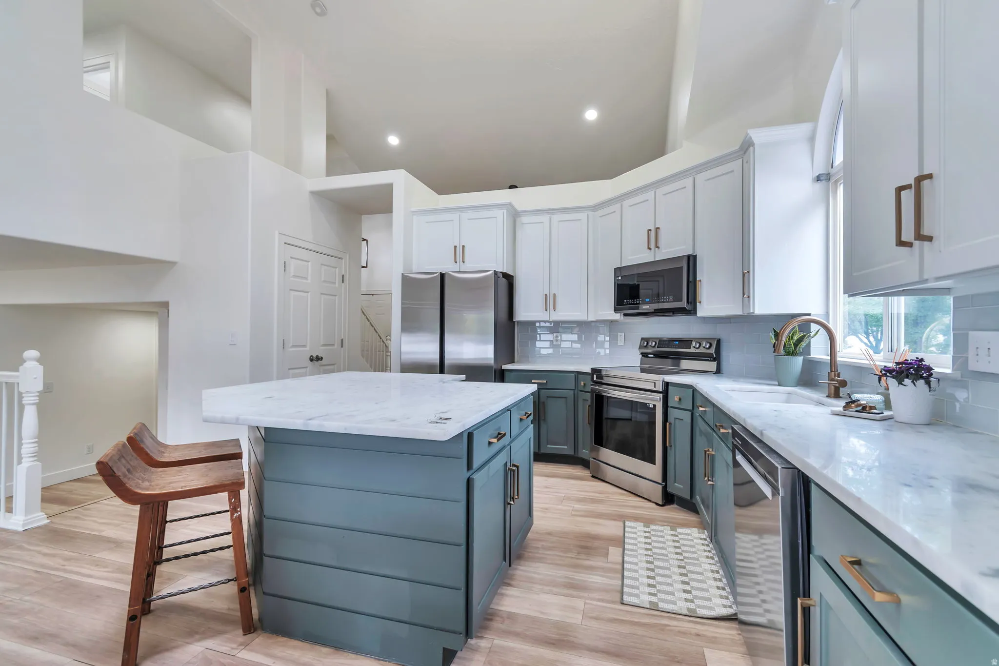 Kitchen featuring a central island with a light-toned countertop, stainless steel appliances, white upper cabinetry, and blue-toned lower cabinetry