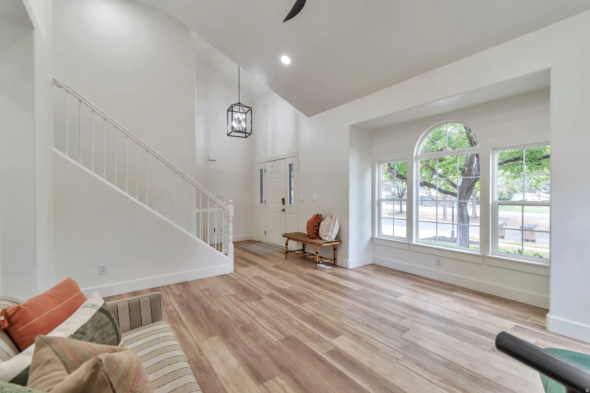 Spacious entryway featuring high vaulted ceilings, wood-finish flooring, a prominent staircase, and large windows with an arched central pane