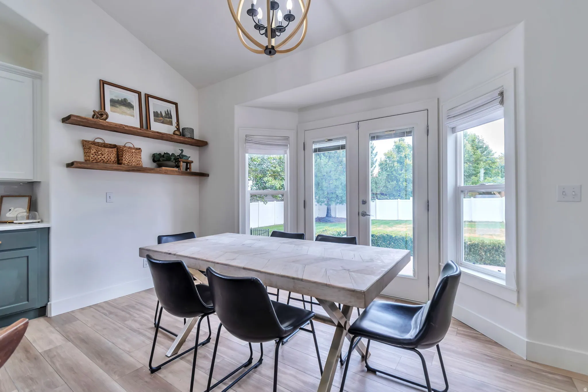 Vaulted ceiling with an overhead light fixture, wood-finish flooring, and a bay window featuring a double glass-panel door