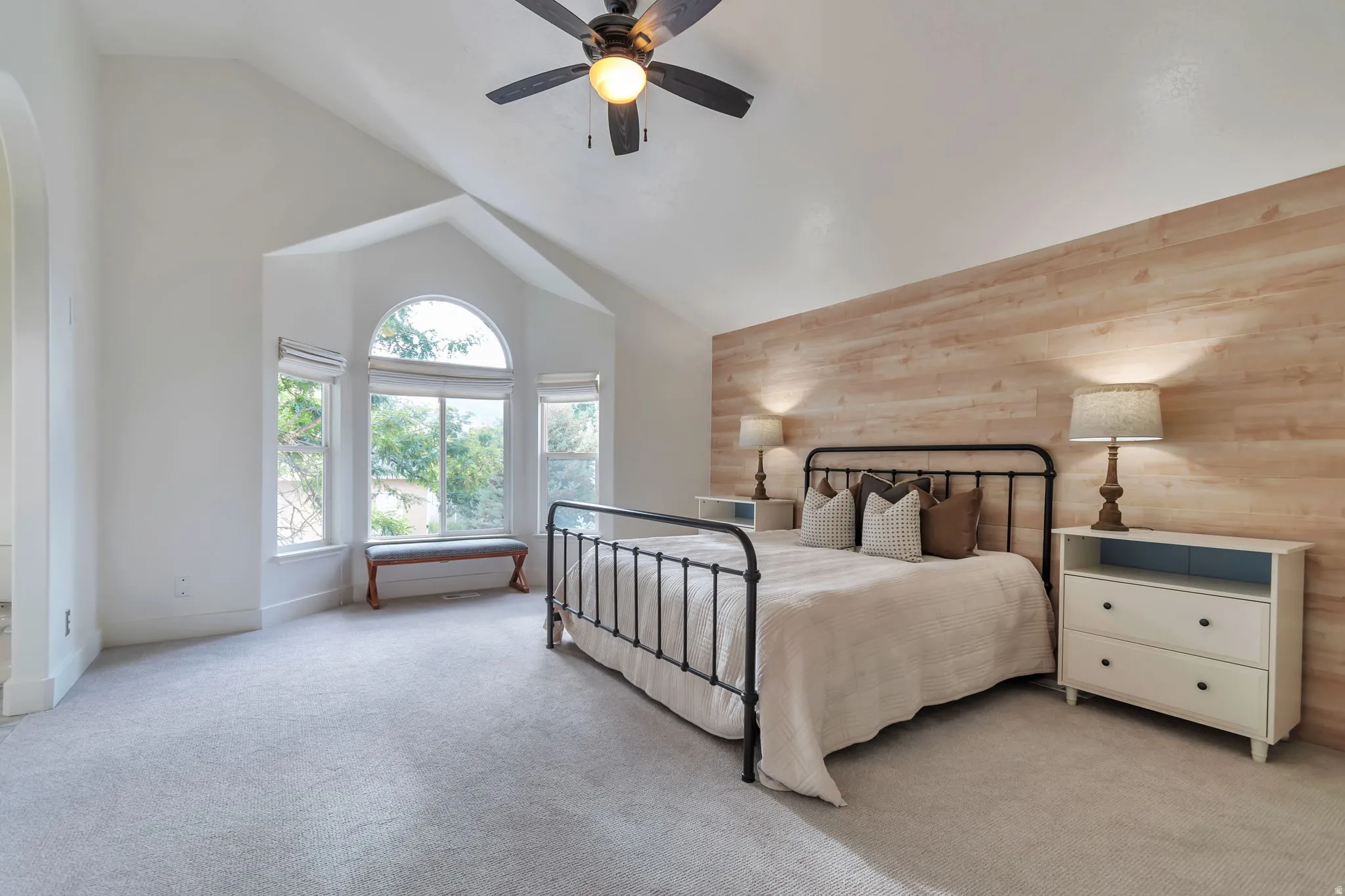 Vaulted ceiling with a ceiling fan, arched window, three panel windows, light wood-finish accent wall, and light-toned carpeting