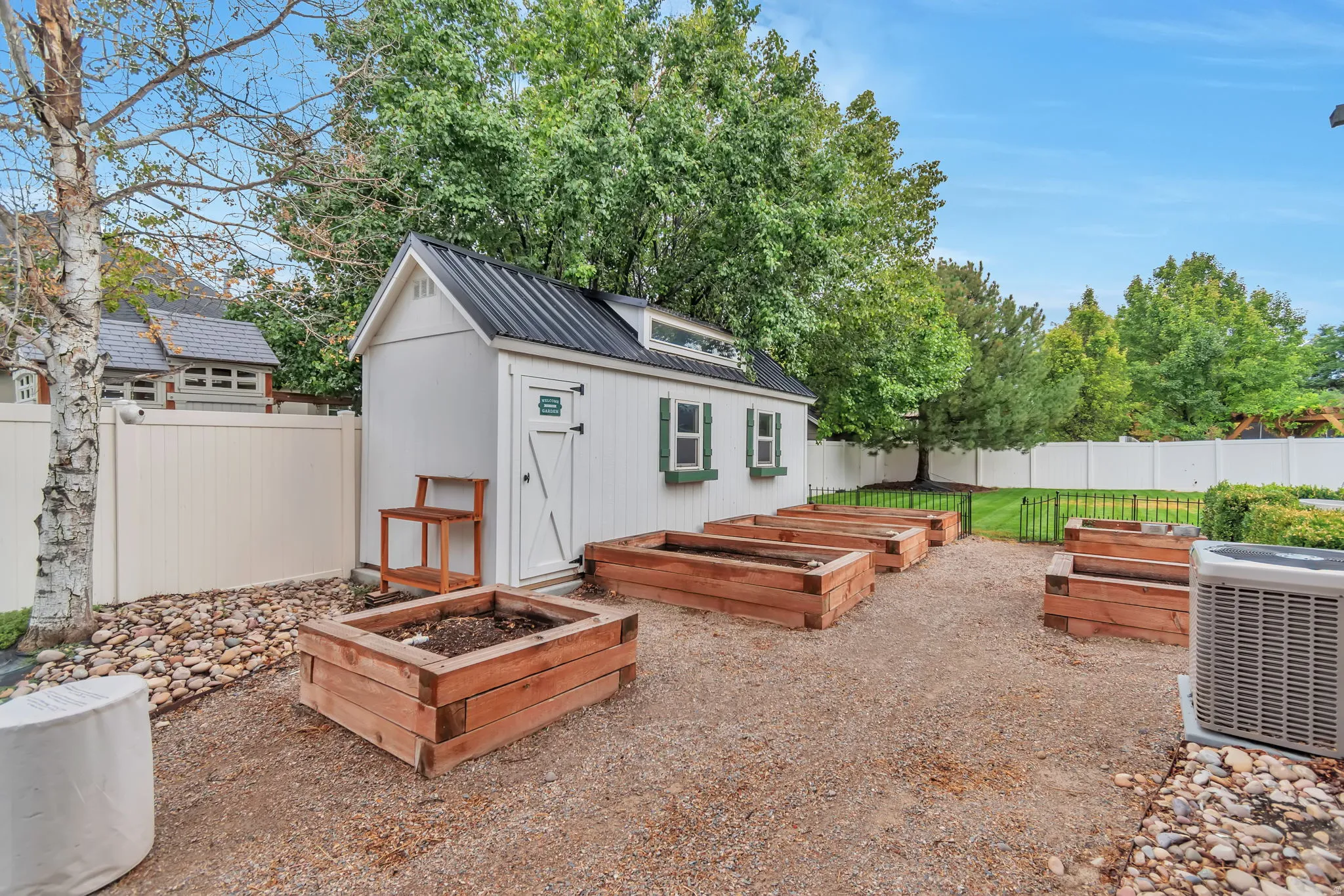 White storage shed with a black metal roof, raised garden beds, and gravel landscaping