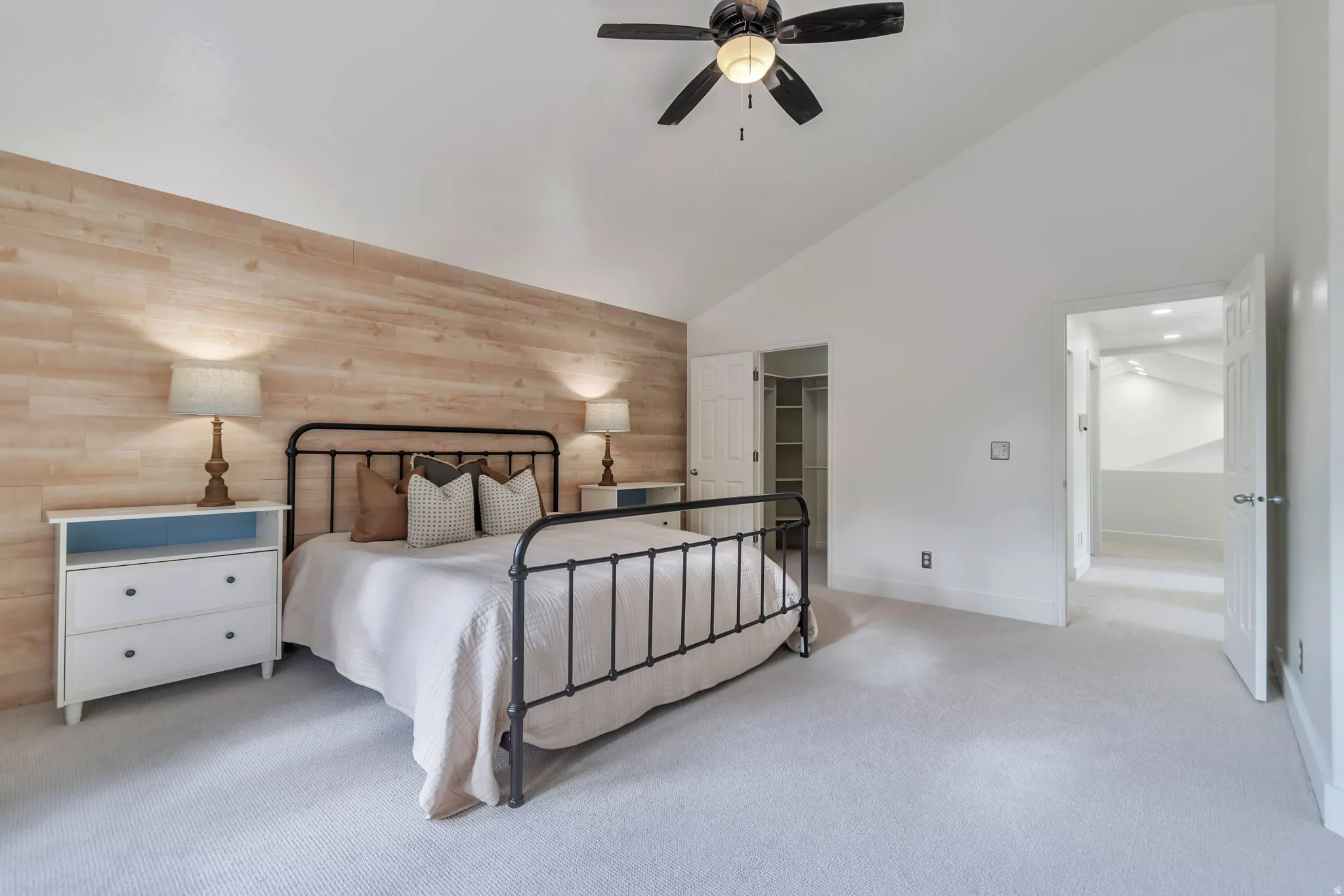 Vaulted ceiling with a ceiling fan, light wood-finish accent wall, and plush carpet flooring