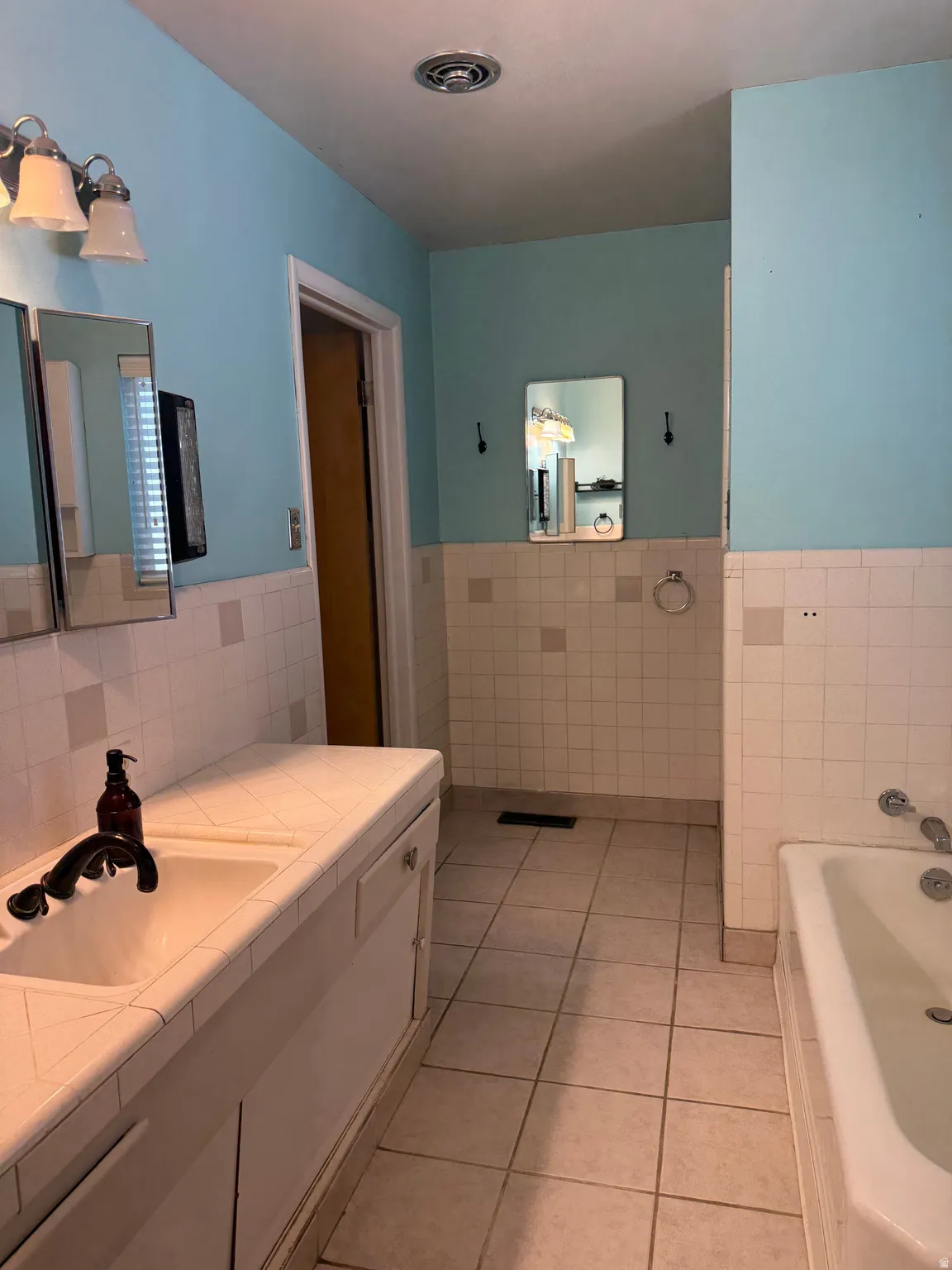 Bathroom featuring a double vanity with integrated sinks, tile countertop, and white cabinetry