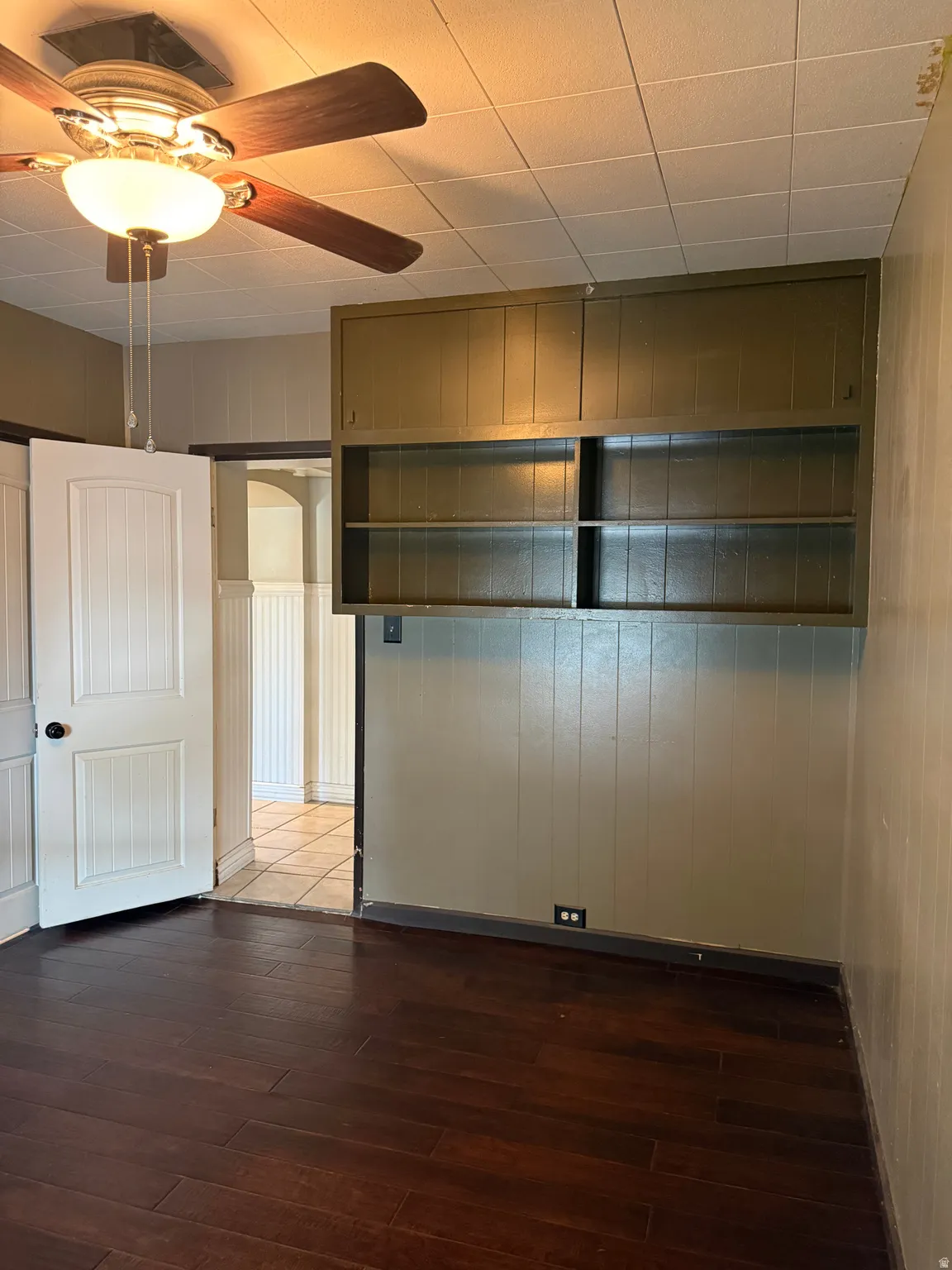 Room featuring dark wood-finish flooring, a ceiling fan with integrated lighting, and a white paneled door