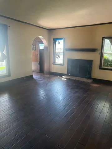 Dark wood-finish flooring, arched doorway, classic fireplace with mantel, and dark trim details