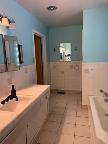 Bathroom featuring a double vanity with integrated sinks, tile countertop, and white cabinetry