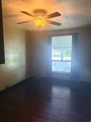 Dark wood-finish flooring, ceiling-mounted fan with integrated light fixture, and a window with an external awning