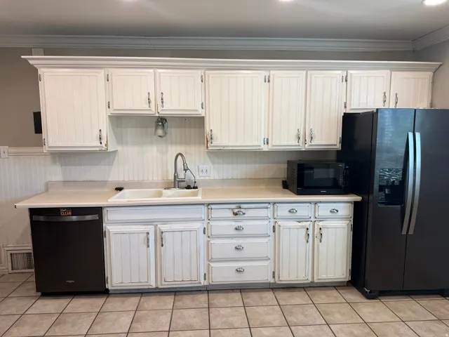 Kitchen featuring white cabinetry with crown molding, beadboard backsplash, light-toned countertops, a double basin sink with a gooseneck faucet, and tile flooring