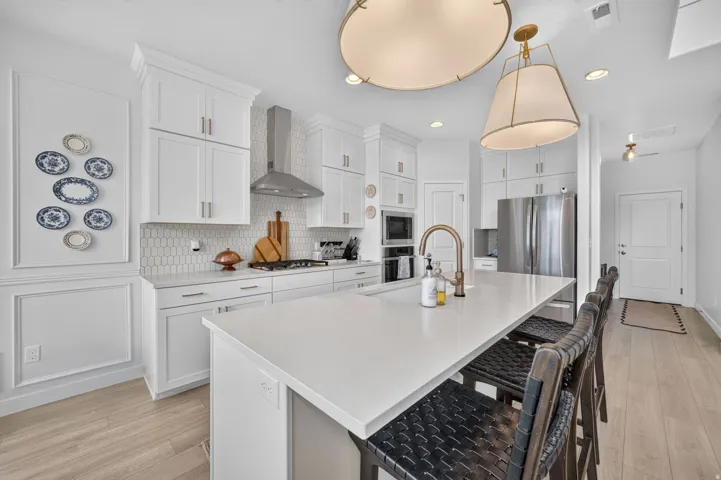 White shaker cabinetry, honeycomb tile backsplash, stainless steel appliances, solid surface countertops, and wood-finish flooring