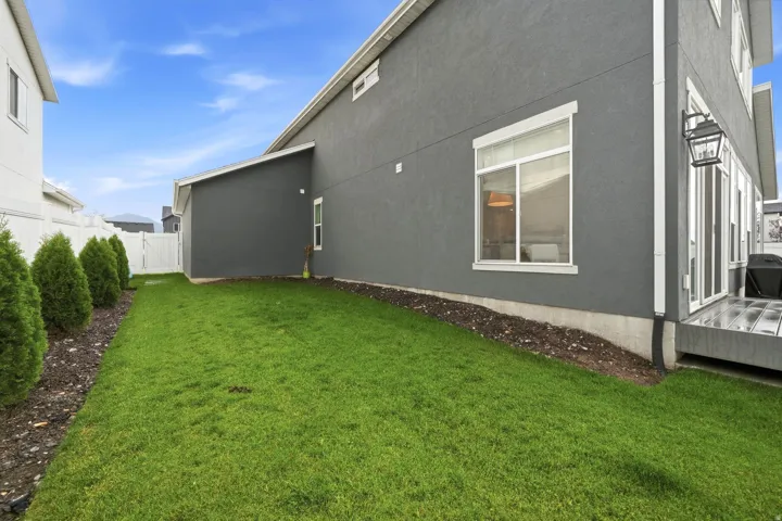 Manicured lawn with mature evergreen plantings, a privacy fence, and a built-in outdoor lantern