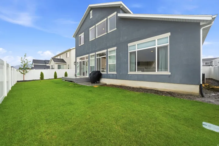Expansive green lawn with a white vinyl fence, rear exterior with multiple windows, and a wood-finish deck