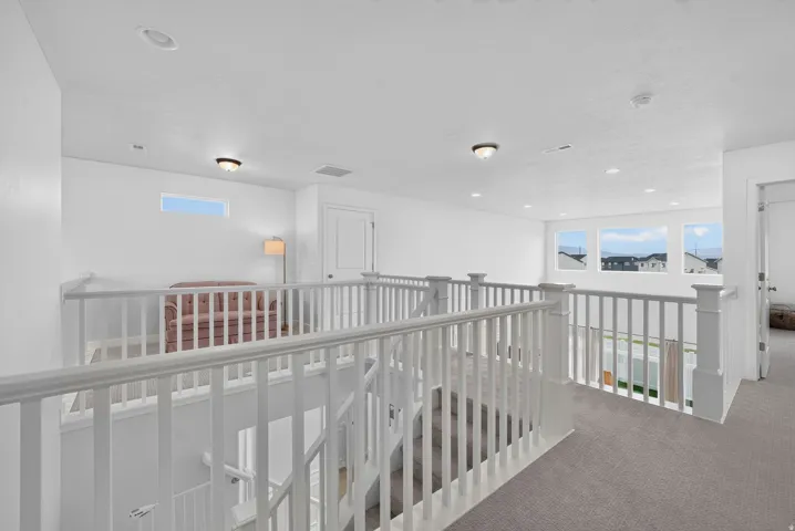 Carpeted upper level featuring white railings, recessed lighting, and multiple windows