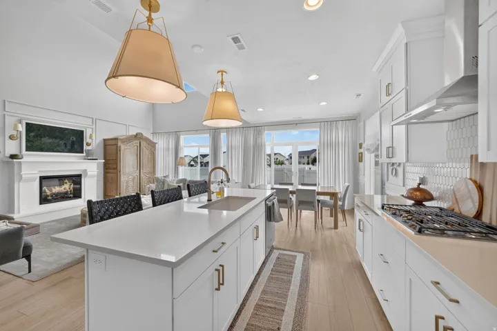 Open-concept kitchen featuring an expansive island with seating, a gas range with a stainless steel range hood, and white shaker cabinetry