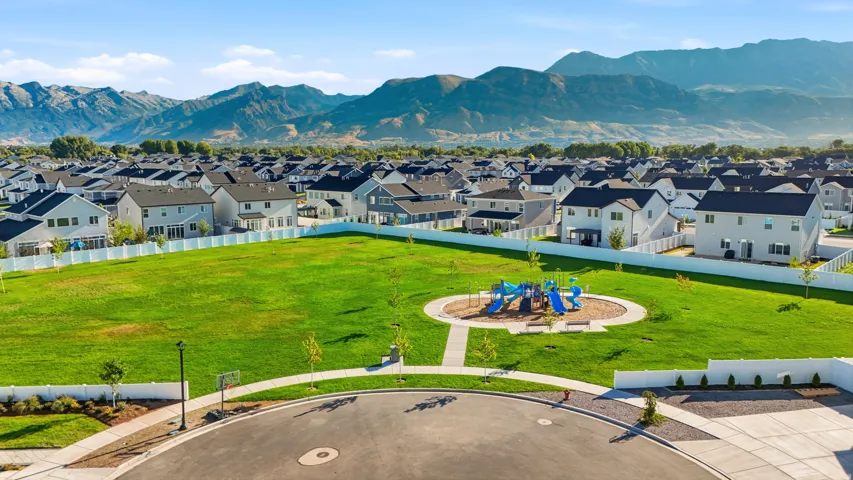 Expansive green space featuring a playground, paved pathways, surrounding residential properties, and distant mountain ranges