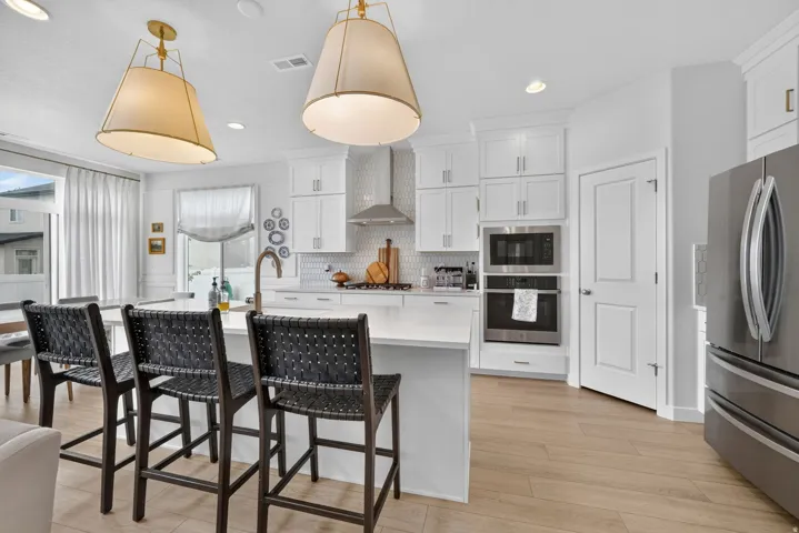 White cabinetry with gold-tone hardware, stainless steel appliances, central island with seating, light wood-finish flooring, and recessed lighting