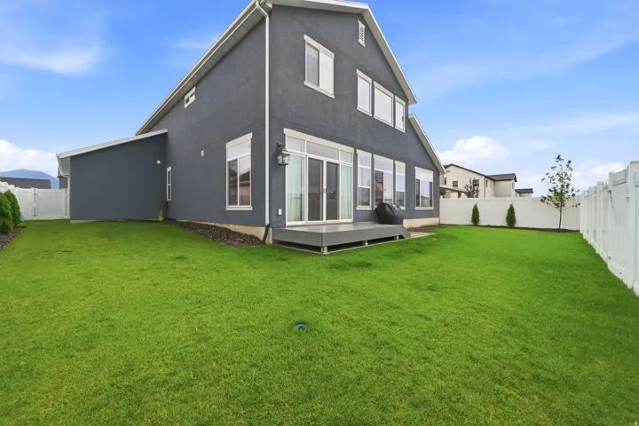 Expansive green lawn, white privacy fencing, ground-level deck, sliding glass doors, and multiple windows