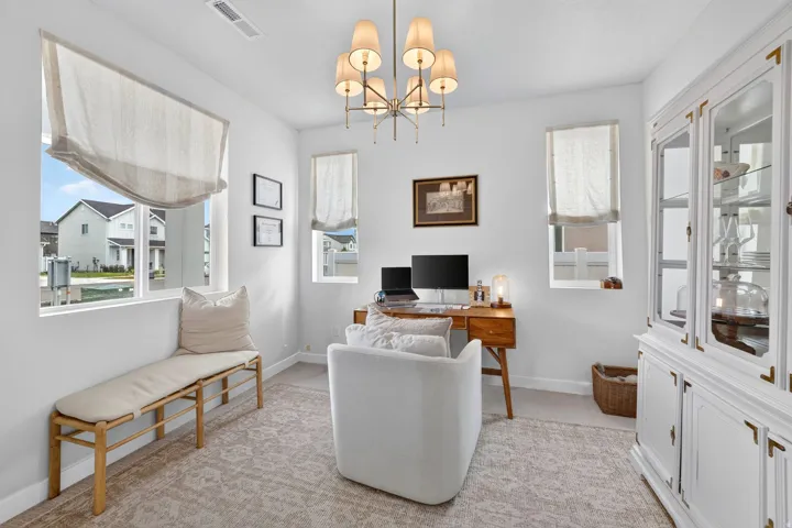 Recessed lighting and a multi-arm chandelier illuminate this space featuring multiple windows