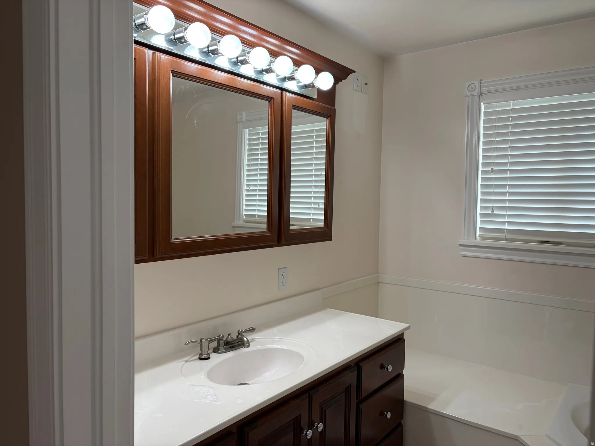 Bathroom featuring a dual-sink vanity with white quartz countertop, wood-finish cabinetry, and polished chrome faucetry