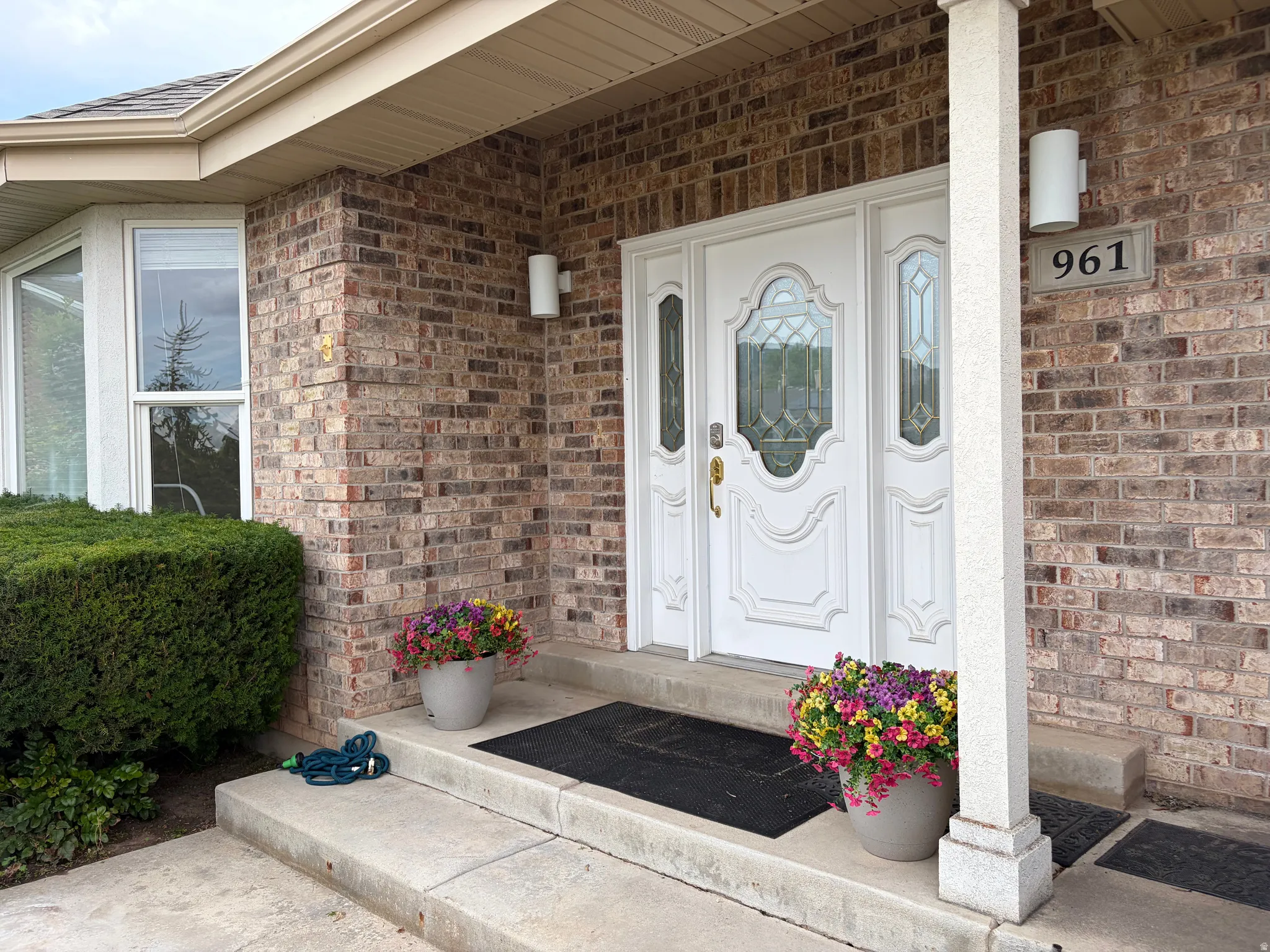 Brick exterior with a prominent white entry door featuring decorative glass inserts, a bay window, and a covered entryway with a column