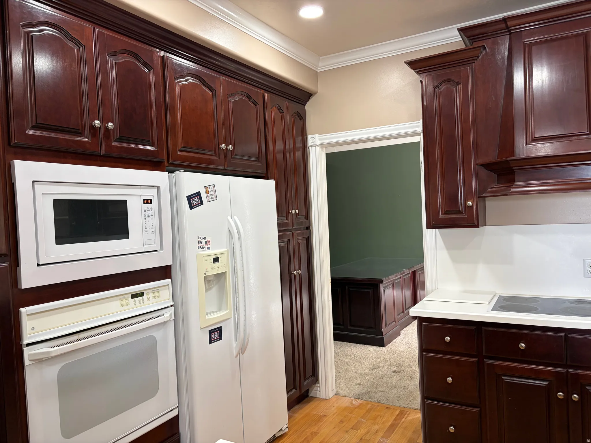 Rich wood-finish cabinetry with decorative molding, white built-in oven, white microwave, white side-by-side refrigerator, and light-toned countertops