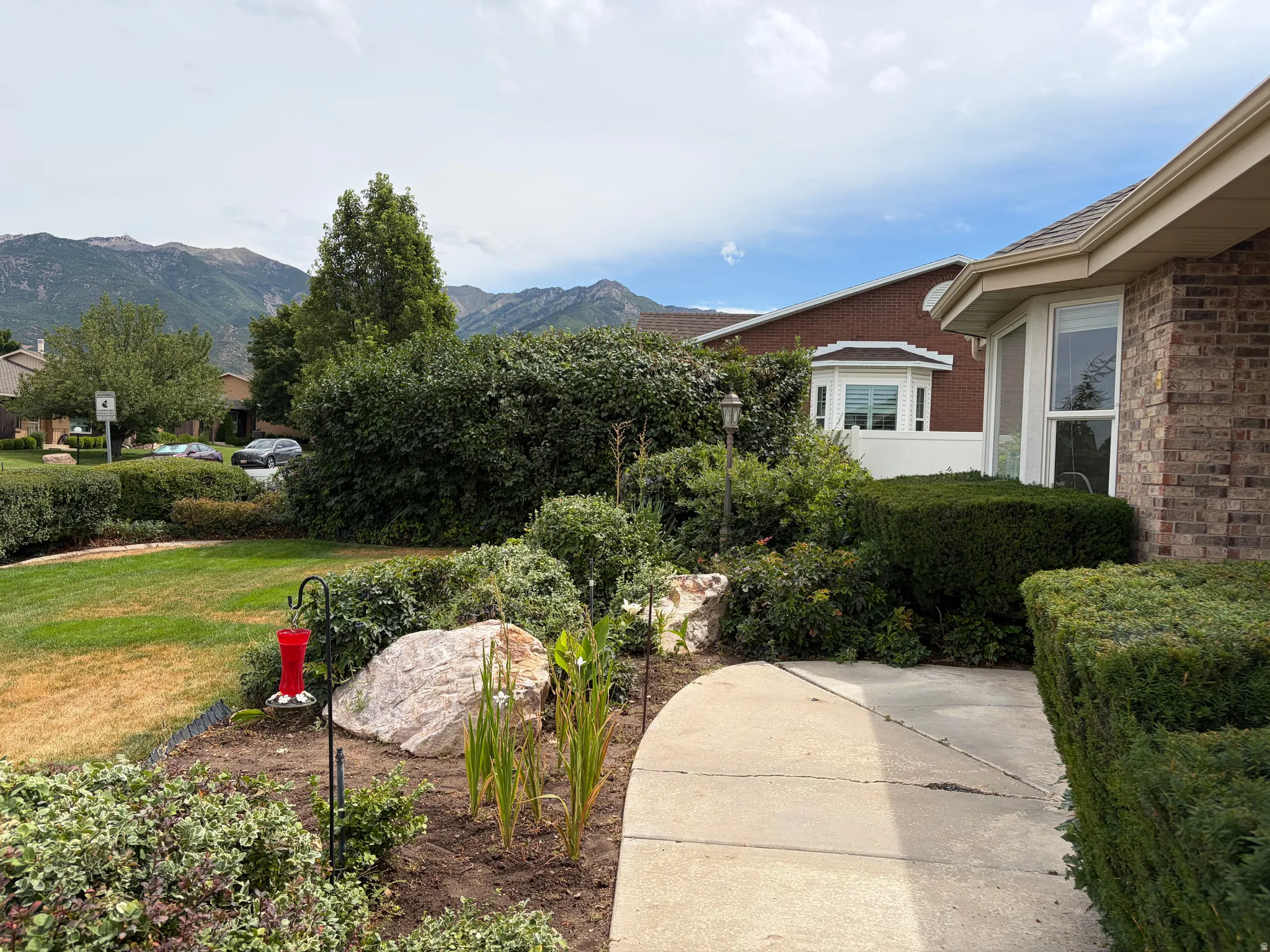 Brick exterior with multiple bay windows, established landscaping, concrete pathway, and mountain backdrop