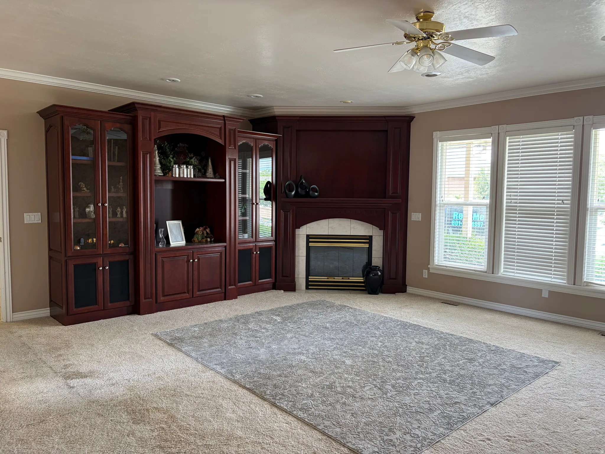 Custom built-in cabinetry, integrated fireplace with tile surround, multiple windows with blinds, crown molding, and a ceiling fan with light fixture