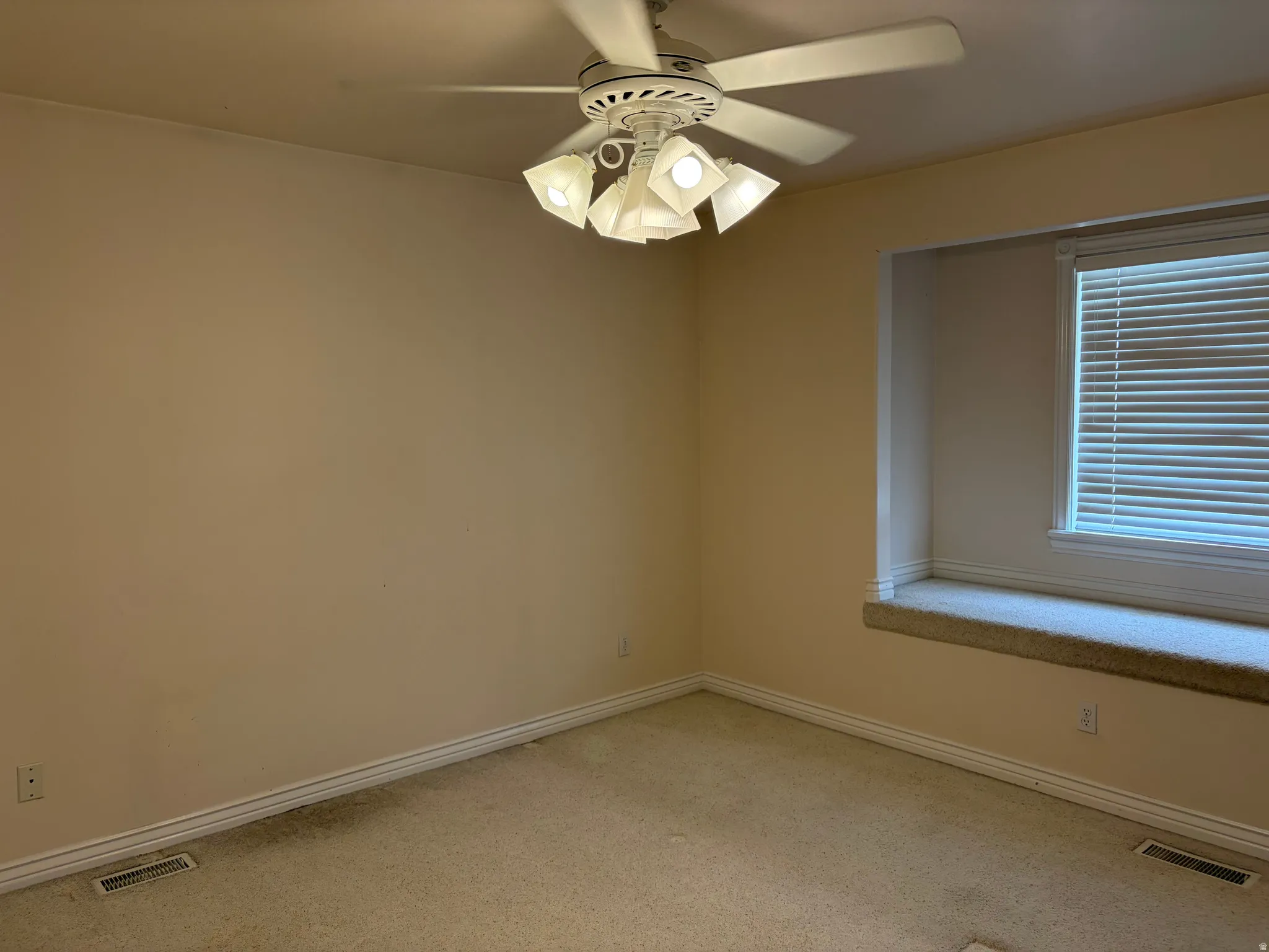 Recessed window with a built-in window seat, ceiling fan with integrated lighting, and neutral carpet flooring