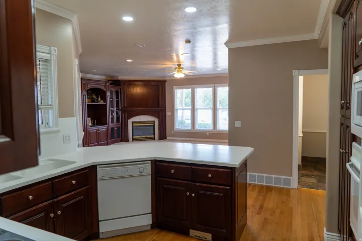 Kitchen island with a white countertop and dark wood-finish cabinetry, recessed lighting, hardwood flooring, built-in fireplace with white tile surround, and multiple windows