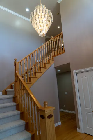 Two-story foyer featuring a chandelier, wood staircase with carpeted treads, and wood-finish flooring