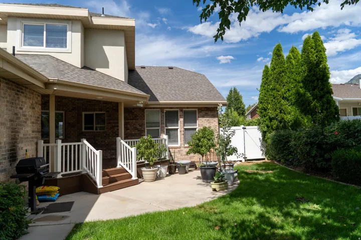 Brick exterior with covered patio, concrete hardscaping, and a lush lawn