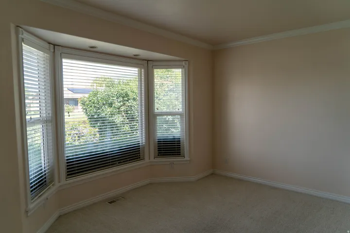 Bay window with integrated recessed lighting, crown molding, baseboard trim, and wall-to-wall carpeting