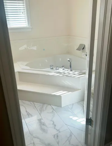Corner soaking tub with a tiled surround, chrome fixtures, and a handheld showerhead
