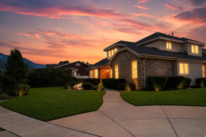 Brick and stucco exterior, arched entryway, concrete walkway, manicured lawn, and mature landscaping