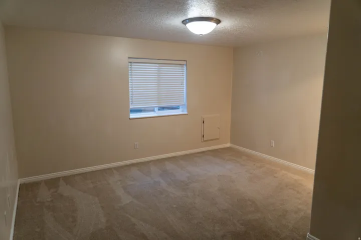 Neutral-toned carpeting, window with horizontal blinds, flush mount ceiling light fixture, and light-colored wall paint