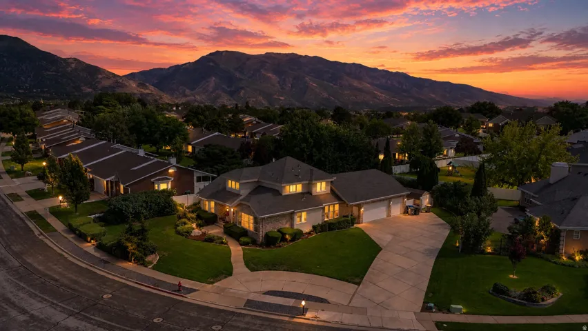 Expansive concrete driveway, mature landscaping, and an attached two-car garage
