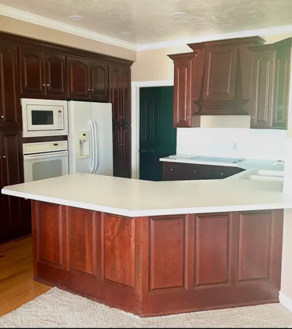 Kitchen featuring rich wood cabinetry, integrated white appliances, light-toned countertops, and crown molding accents