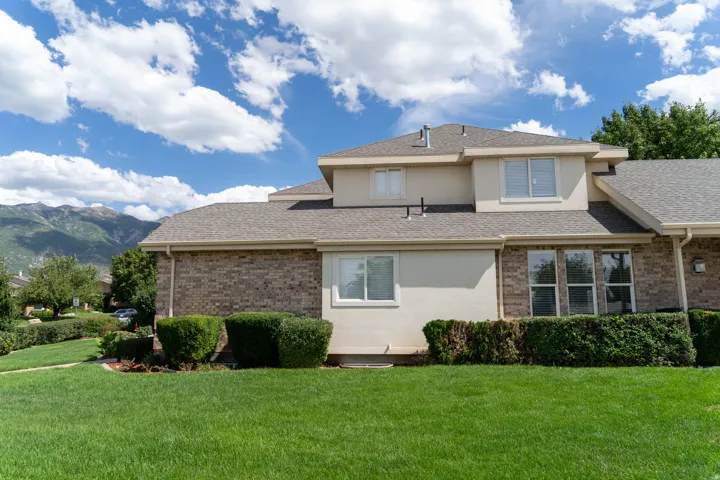 Manicured lawn with established landscaping, brick and stucco exterior, multiple windows, and a mountain backdrop