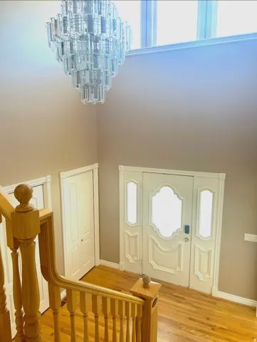 Grand entryway with a multi-tiered glass chandelier, light wood-finish flooring, and a decorative frosted glass entry door
