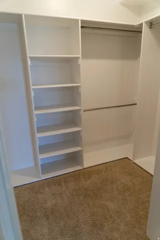 Built-in custom closet system featuring white shelving, multiple hanging rods, and neutral-toned carpeting