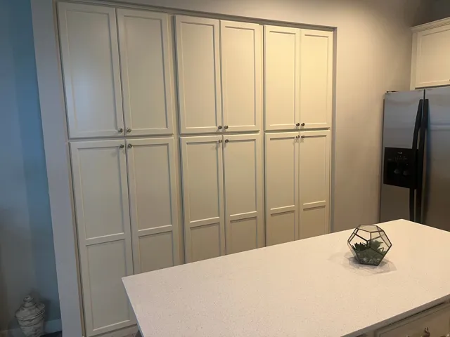 Floor-to-ceiling cabinetry with panel doors, stainless steel refrigerator, and a light-toned countertop