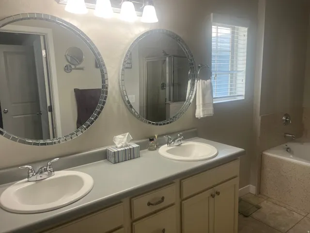 Dual vanity with undermount sinks, round mosaic-framed mirrors, and a built-in bathtub with tiled surround