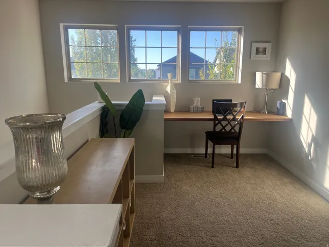 Carpeted open loft area featuring a built-in wood-finish desk, three transom windows, and a partial wall with railing