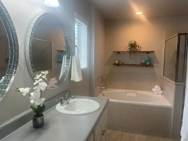 Built-in soaking tub, glass-enclosed shower, dual vanity with round tiled mirrors, and wood-finish shelving