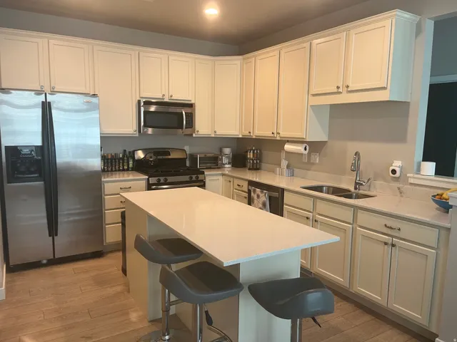 Kitchen featuring stainless steel appliances, wood-finish flooring, a double basin sink, and a center island with countertop seating